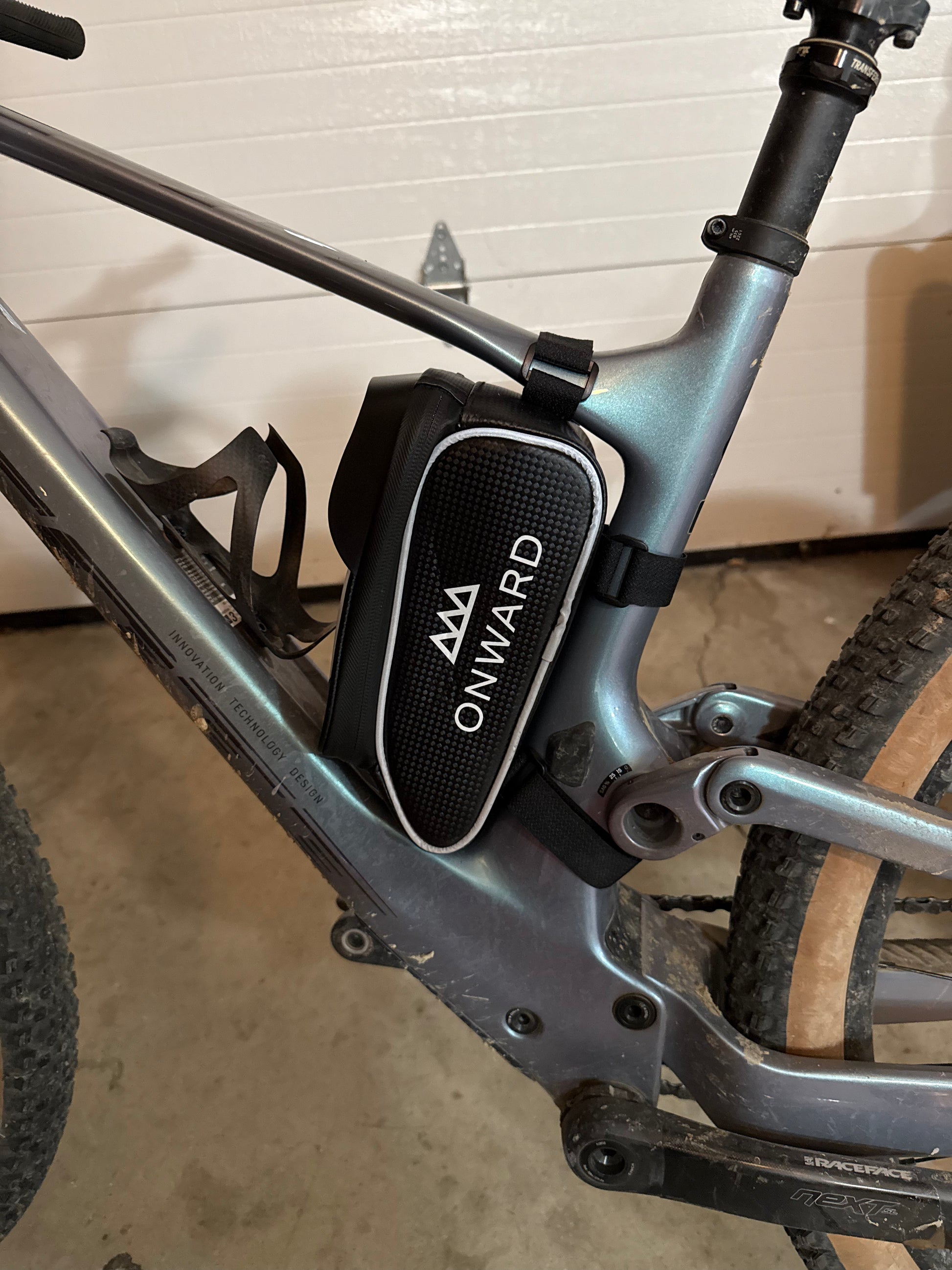 Bicycle with an 'Onward' device attached to the frame against a white wall.