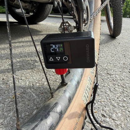 Digital tire pressure monitor attached to a bicycle wheel on a road.