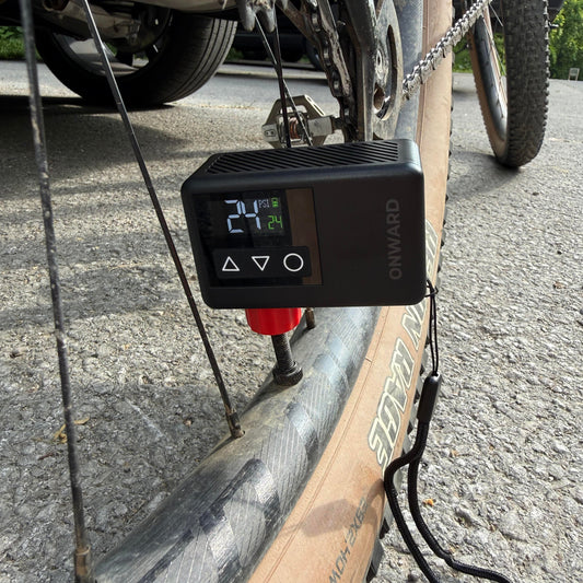 Digital tire pressure monitor attached to a bicycle wheel on a road.